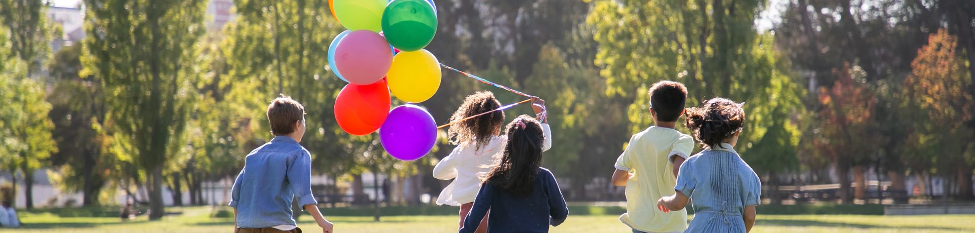 Children running outside, away from the camera, with one child holding colorful balloons.