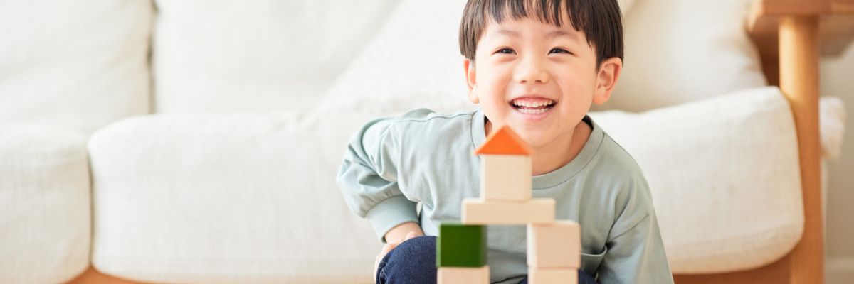 A child looking at the camera and smiling with a stack of toy blocks assembled into a tower.