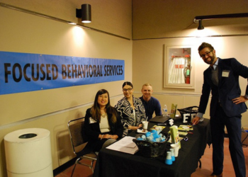 A group of staff tabling an event with informational items available to the public and a blue flier that says "Focused Behavioral Services" on the wall behind them.