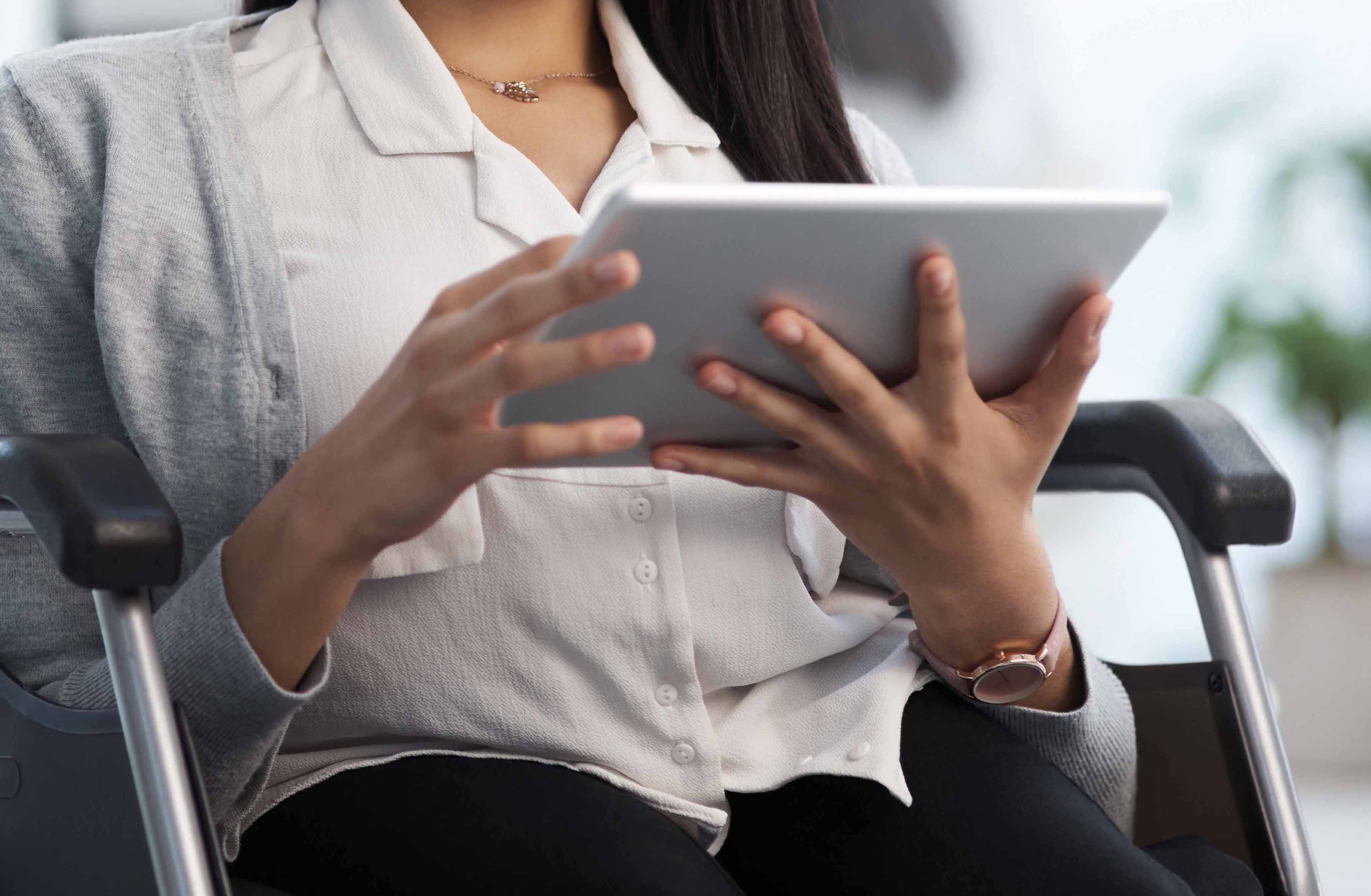 Women sitting in wheelchair holding and using tablet 