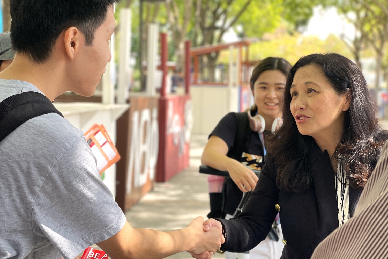 a photograph of an intern introducing himself to Bao and shaking her hand infront of the presidents booth