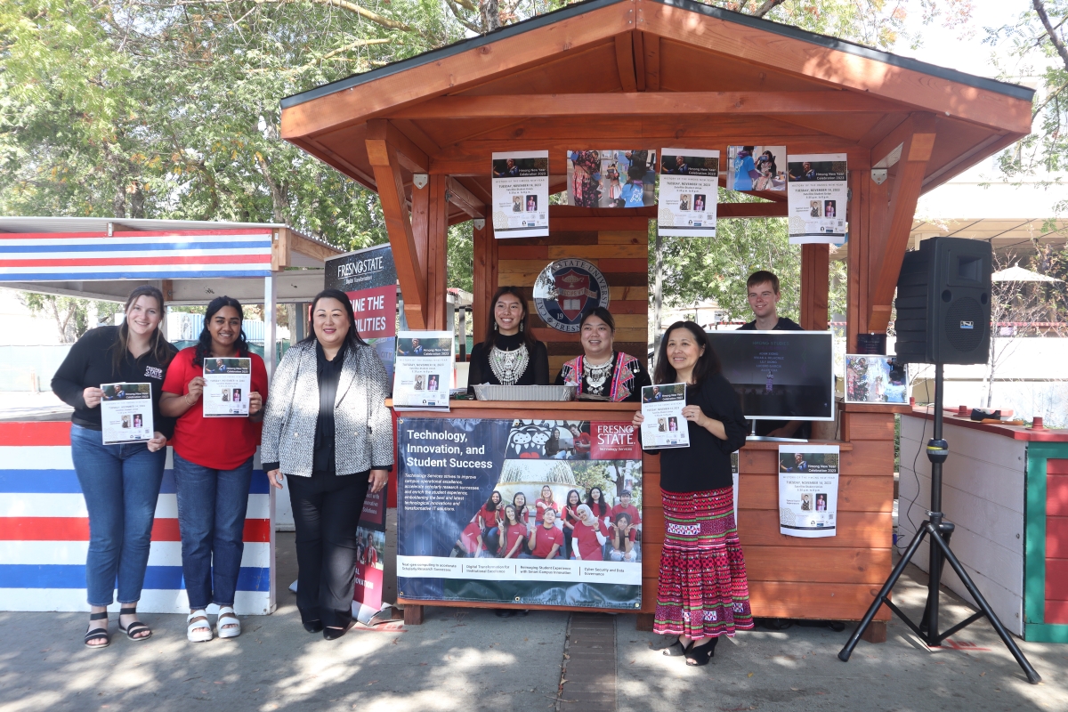 Picture of Bao, DXI staff and interns infront of the presidents booth in Traditional Hmong skirts