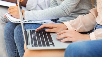 Two individuals working closely, one typing on a laptop and the other writing in a notebook, emphasizing a collaborative or educational environment.