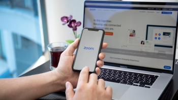 Close-up of hands holding a smartphone with the Zoom app logo on the screen, positioned over a laptop displaying the Zoom website, highlighting tools used for virtual communication and meetings.