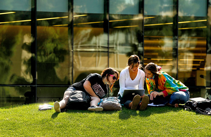 three students sitting on the lawn in front of the library
