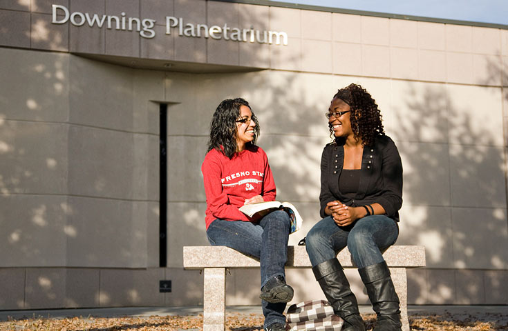 two students sitting on bench outside planetarium