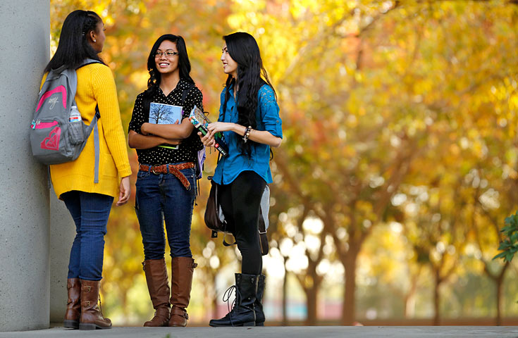 three female students standing next to building in autumn